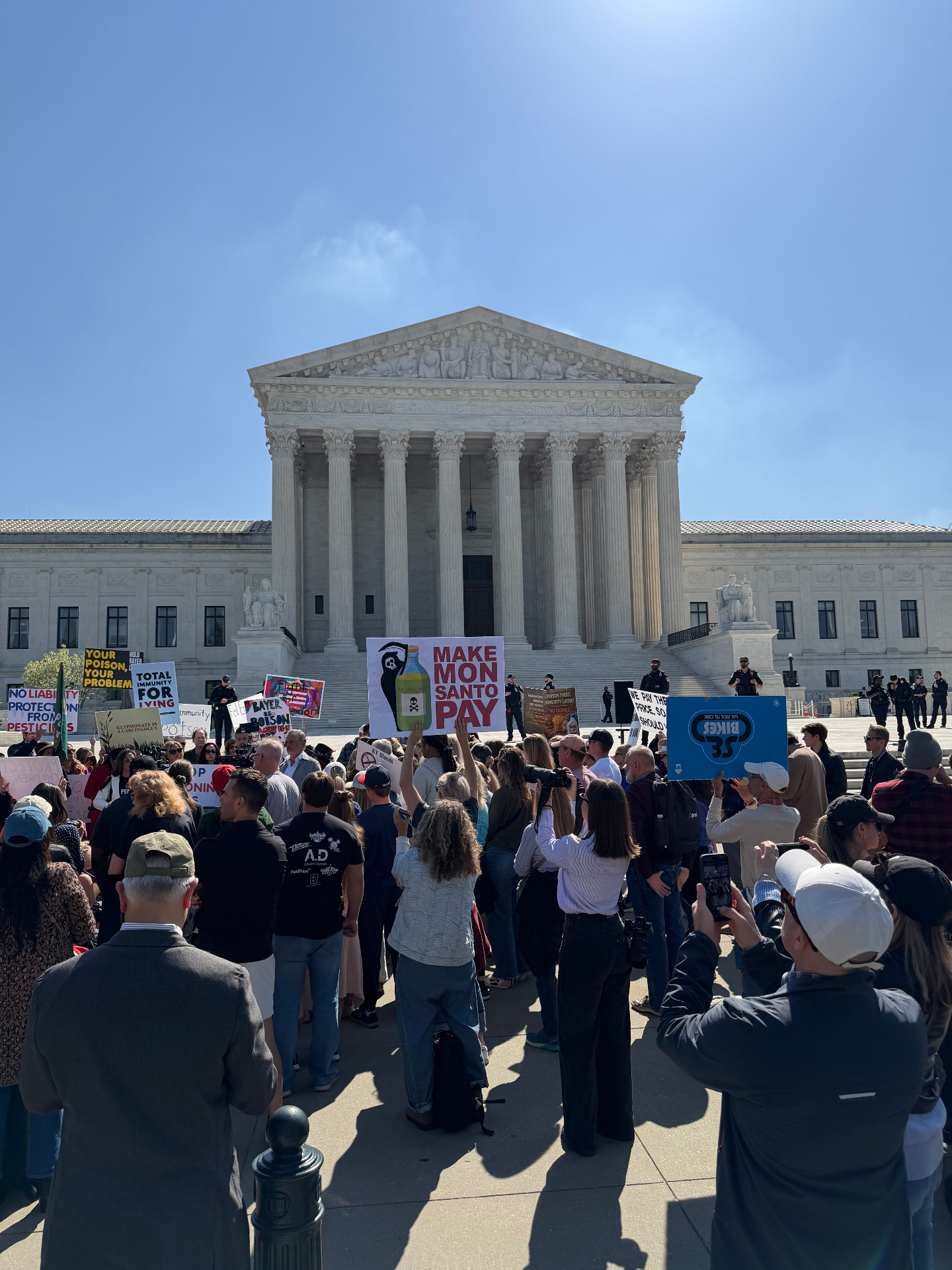 Crowd rallying on the steps of the U.S. Supreme Court with 'Make Monsanto Pay' signs